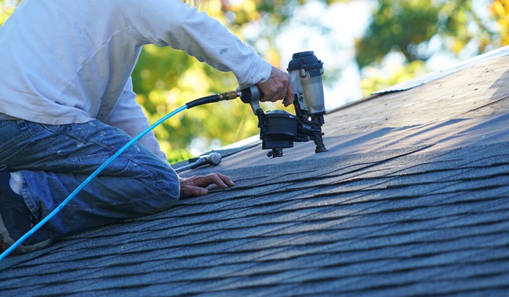 A HAAG certified roof inspector in Louisiana using a nail gun to install asphalt shingles on a sloped roof