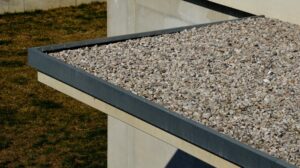 Gravel-covered flat roof with a metal edge and a hint of roof shingles, set against a grassy and concrete background.